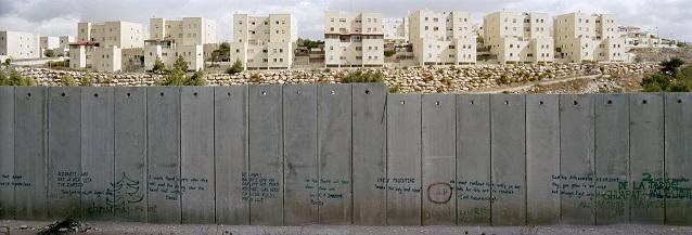 The illegal Israeli settlement of Pisgat Zeev in the Westbank seen from the  Palestinian refugee camp of Shuafat in the outskirts of Jerusalem. Though the separation wall divides the inhabitants of these communities they both hold Jerusalem identity cards. The graviti work is an action of Palestinain artists from Jerusalem. Everybody around the world could contact them and get his quote written on the wall by them. Occupied Palestinian territories, November 2009.
